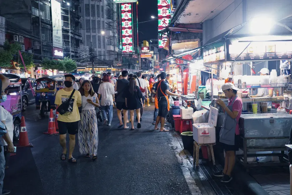Bustling city street market at night with food stalls and people in vibrant setting.
