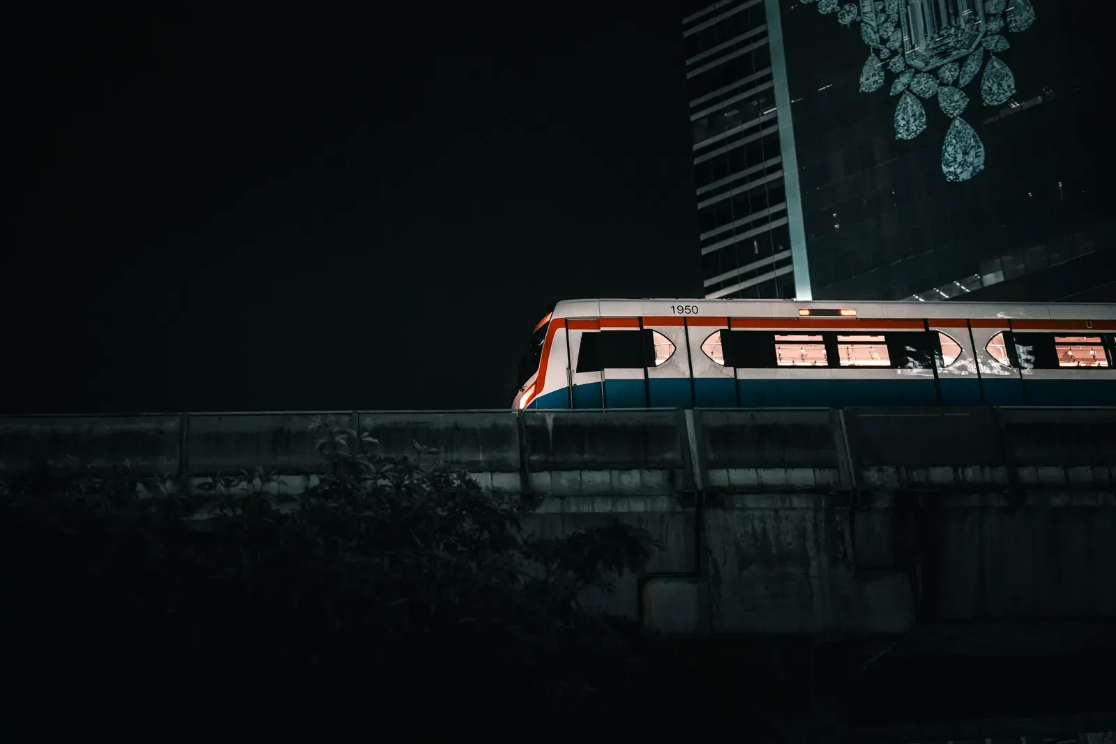 A vibrant urban night scene featuring a Bangkok Skytrain passing by a skyscraper.