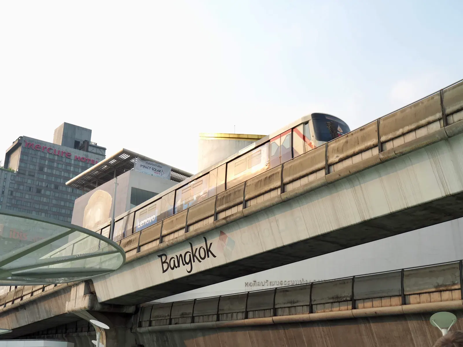 A modern skytrain travels over an elevated track with Bangkok cityscape in the backdrop.