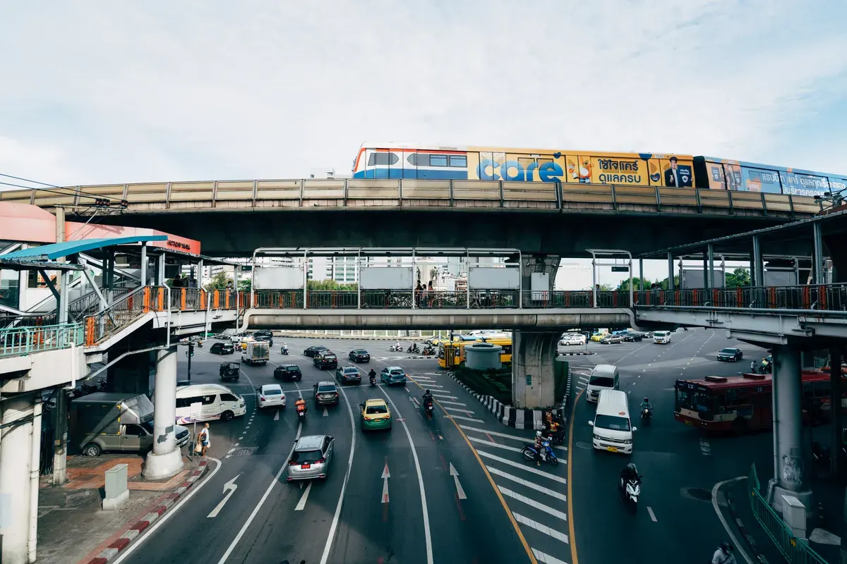 Dynamic cityscape featuring bustling Bangkok traffic with elevated train and highway.