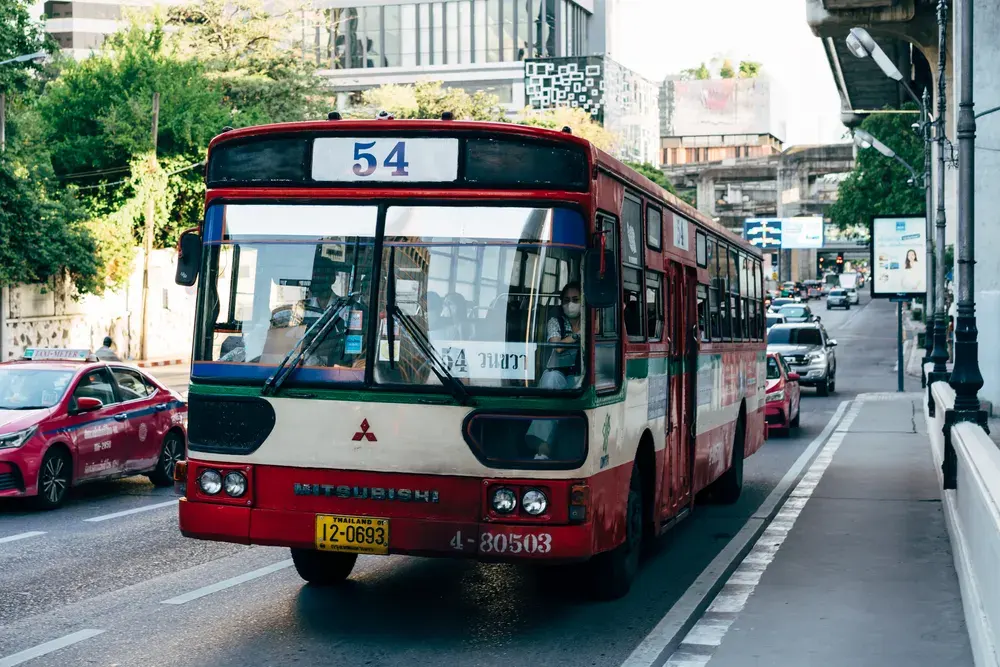 Red bus and bustling city traffic on a sunny day in Bangkok, Thailand.