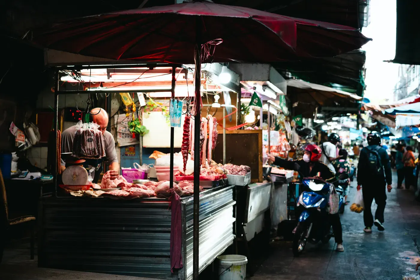Lively street market in Bangkok with people browsing stalls under umbrellas.