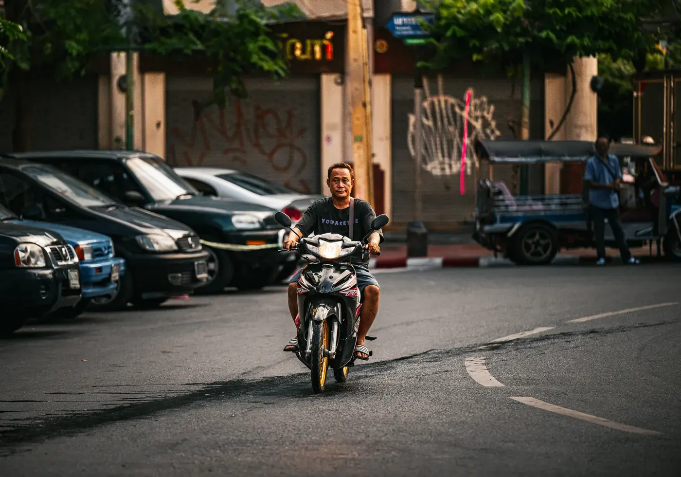 Casual street scene with a man riding a scooter in vibrant Bangkok.