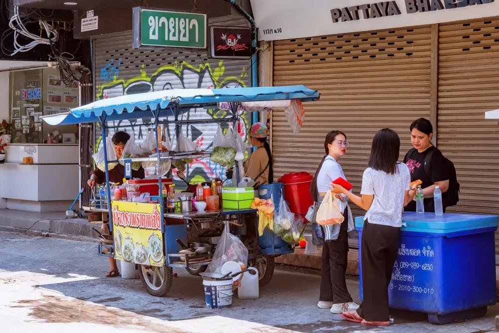 Street food vendor with customers on a sunny day in Pattaya, Thailand, showcasing vibrant urban life.