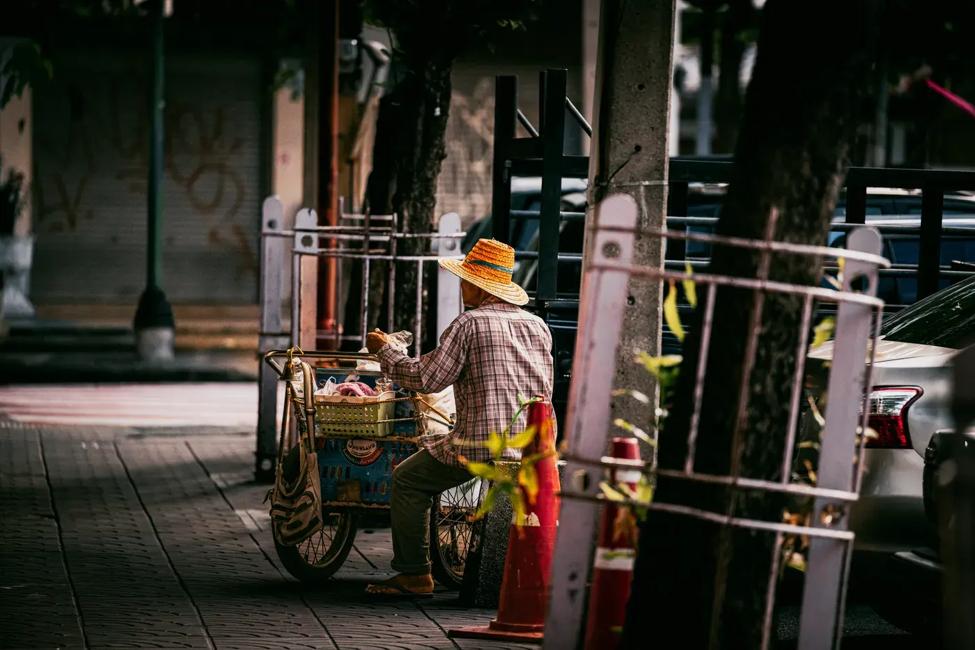 Street vendor with cart selling fresh produce on Bangkok sidewalk on a sunny day.