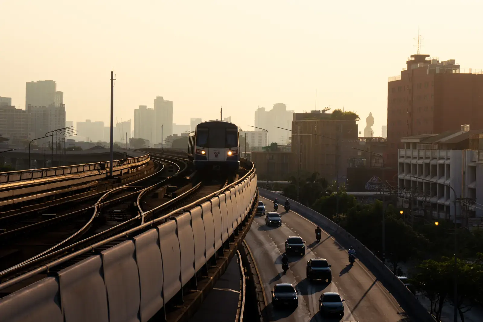 Skytrain navigating urban tracks in Krung Thep Maha Nakhon, offering a scenic view during sunset.