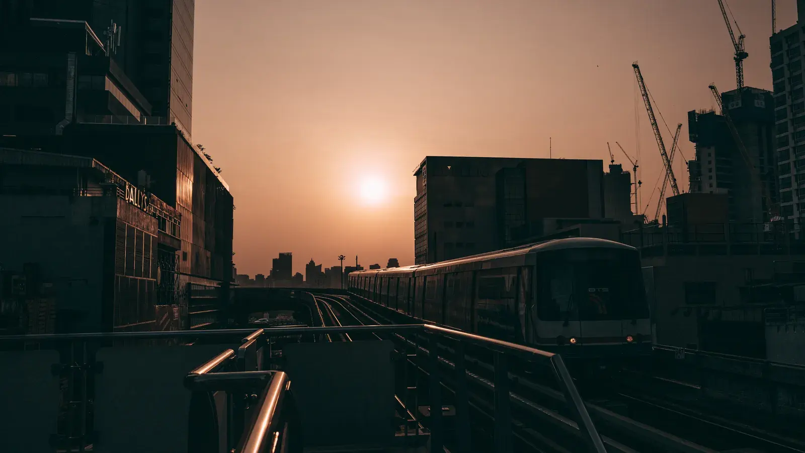 Silhouette of Bangkok skyline at sunset with a train on elevated tracks.