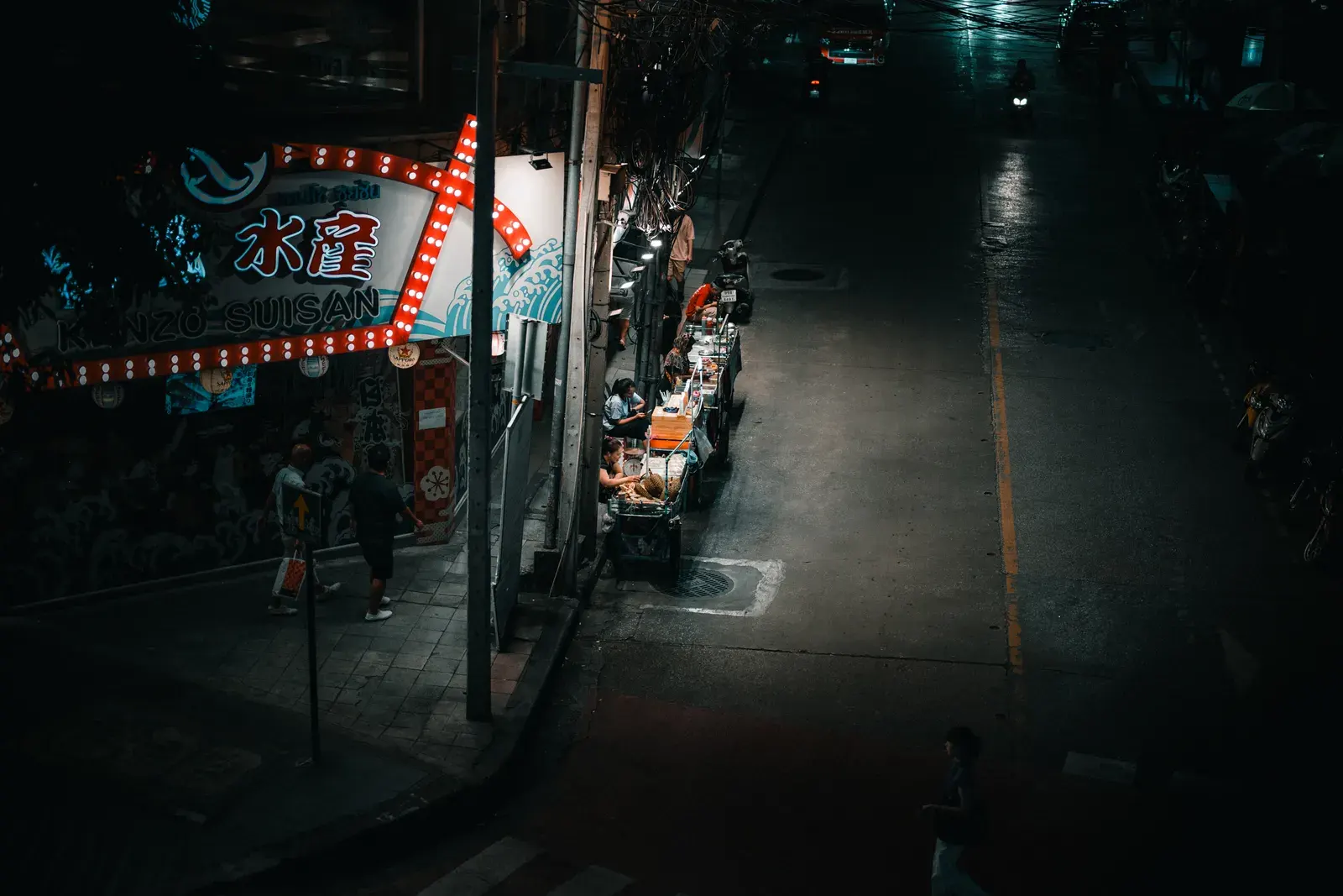 A vibrant street food stall illuminated at night in Bangkok, Thailand, with people enjoying local cuisine.