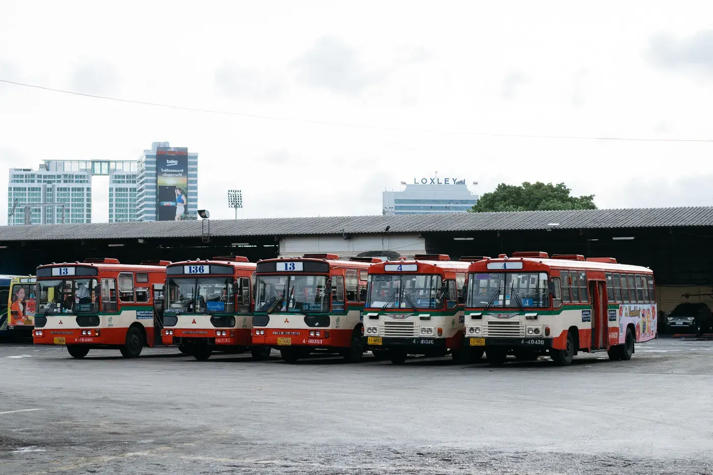 Five public buses lined up at a bus terminal in Bangkok, Thailand.