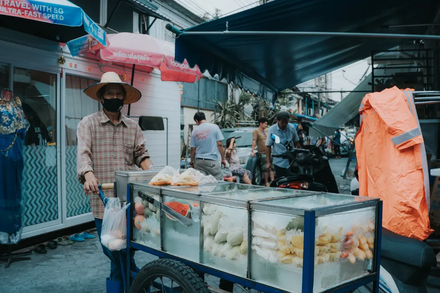 A vendor sells fresh fruit from a cart in a vibrant Bangkok street market.