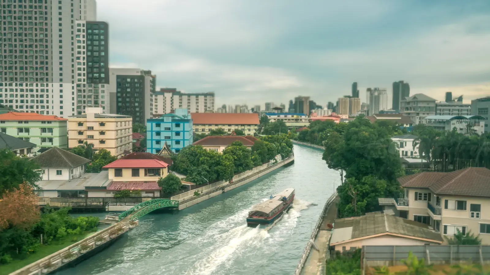 Peaceful canal scene with vibrant buildings and a boat in Bangkok, Thailand.