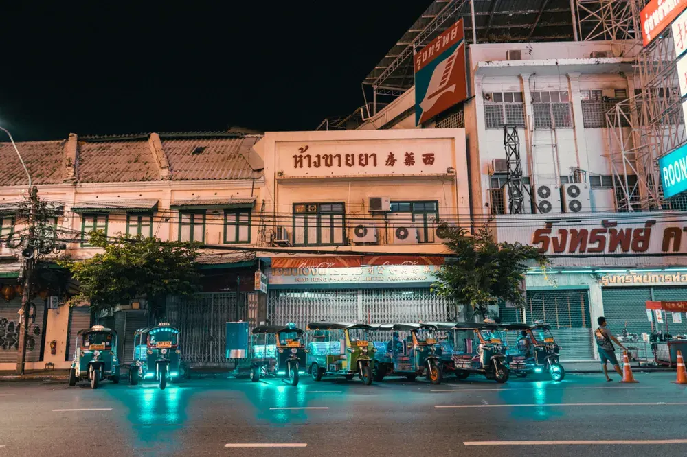 Vibrant night scene featuring electric tuk-tuks parked in front of lit-up city buildings.