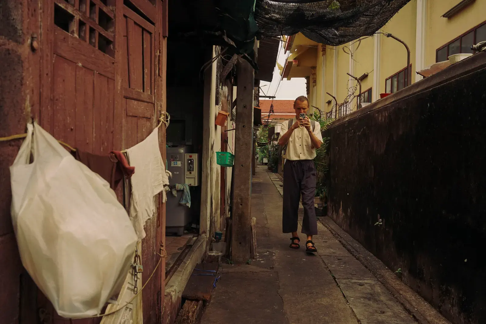 A man uses his smartphone while walking through a narrow alley in Bangkok, Thailand.