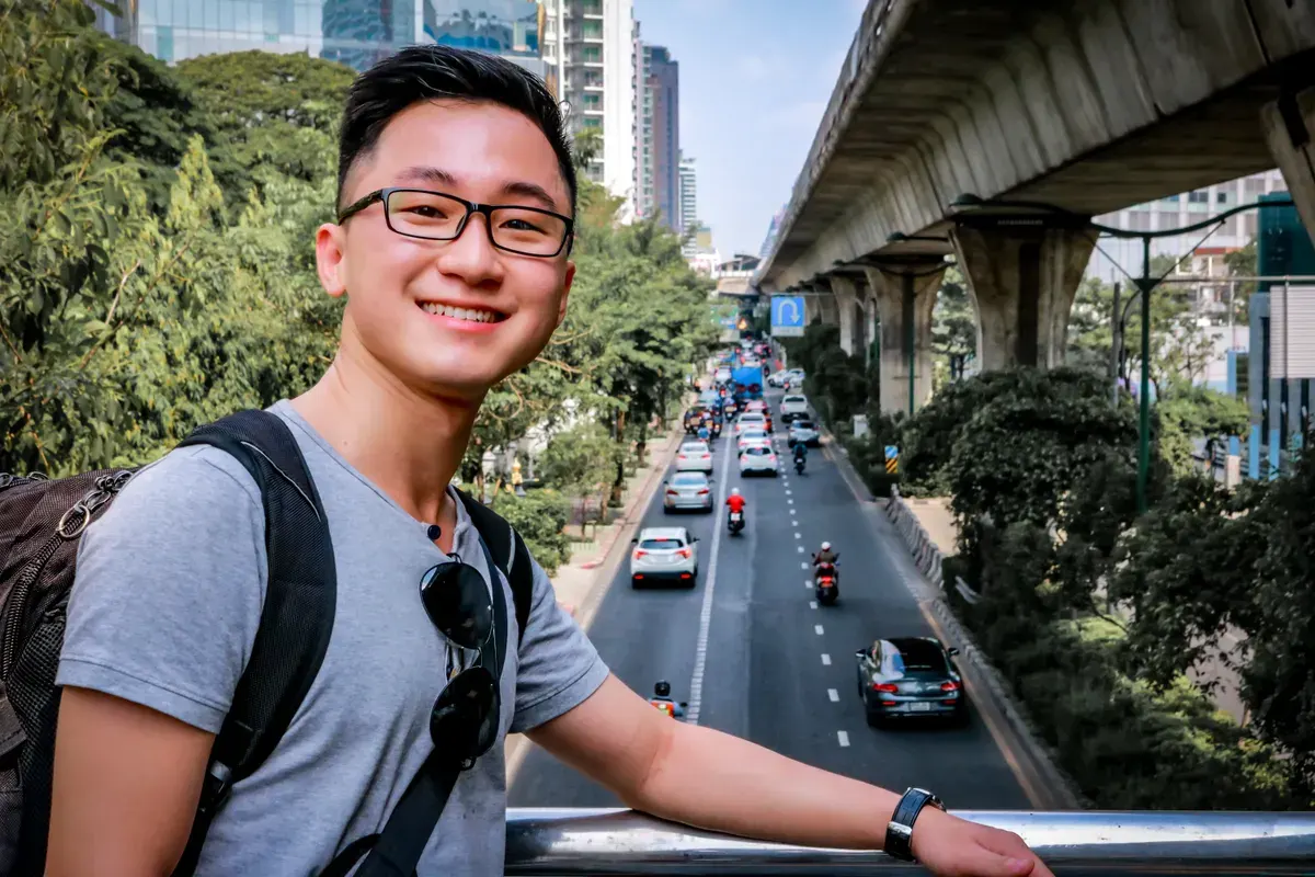 Smiling Asian man on a bridge overlooking urban traffic in Bangkok, Thailand.