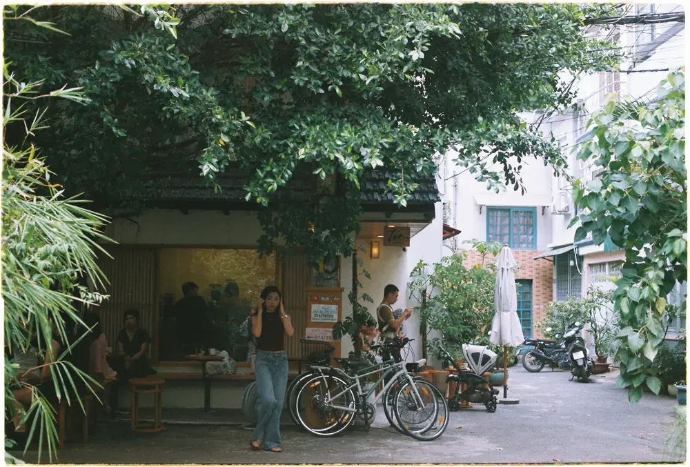 Outdoor café scene with people and bicycles surrounded by greenery.