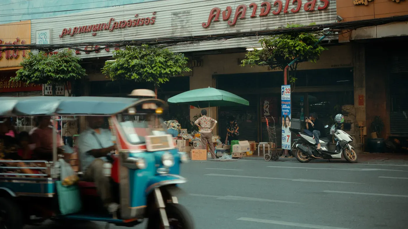 A lively urban scene with a tuk-tuk passing by a traditional storefront, capturing city life.