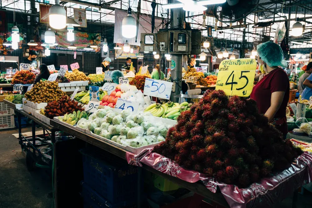 Colorful market stall with exotic fruits and vendors in a bustling Southeast Asian bazaar.
