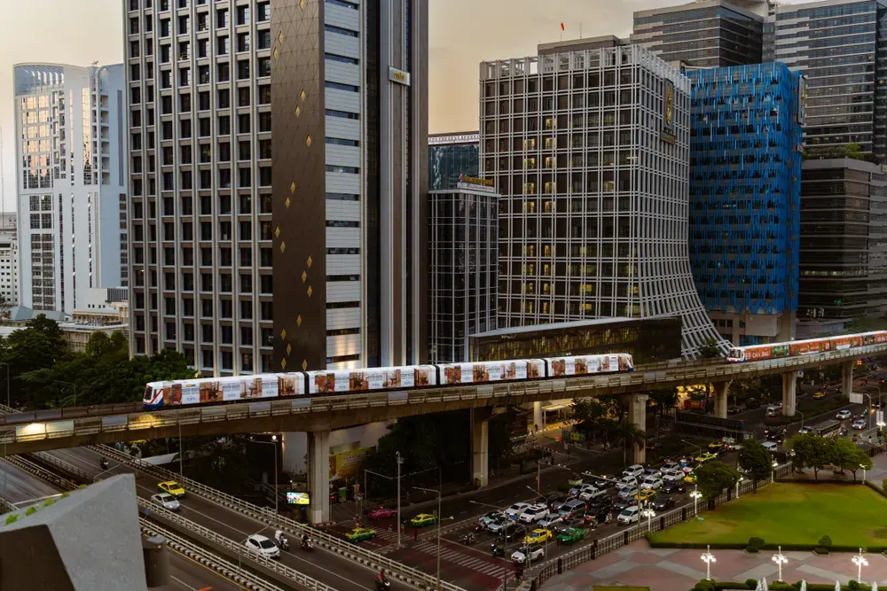 Vibrant Bangkok cityscape featuring illuminated skyscrapers and a passing skytrain during the dusk hours.