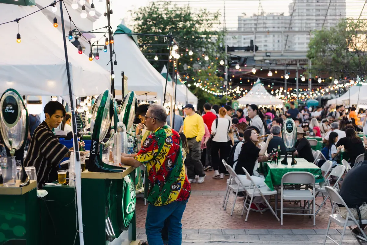 Lively outdoor food festival in Bangkok with bustling crowd and colorful lights.