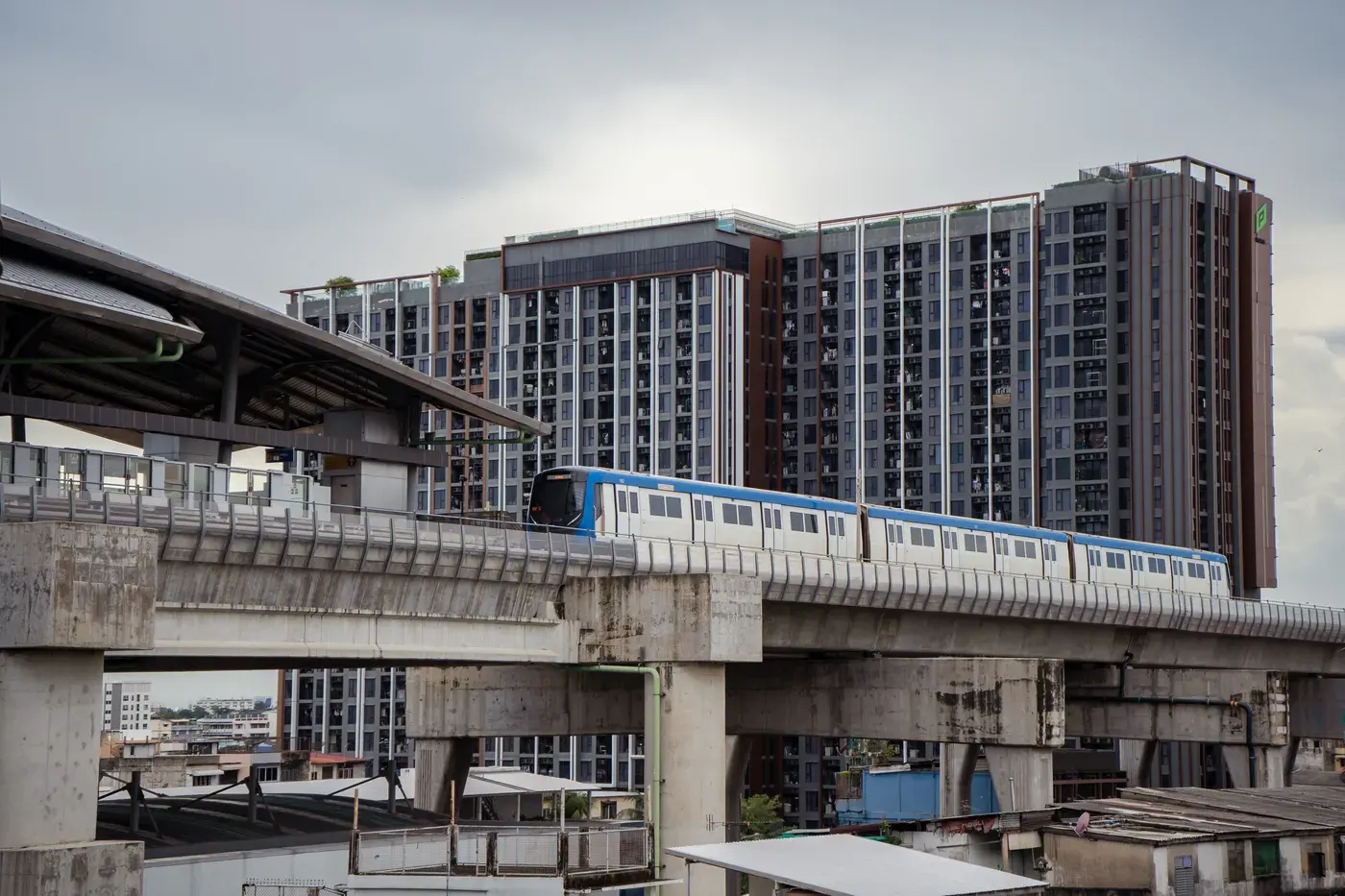 A sky train glides past a modern condominium complex in Bangkok, Thailand, during the daytime.