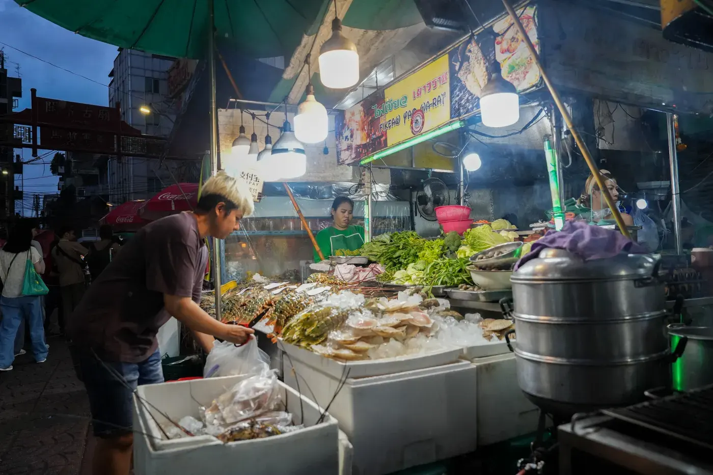 A bustling food stall in Yaowarat Road, Bangkok's Chinatown, offering fresh seafood and vegetables at night.