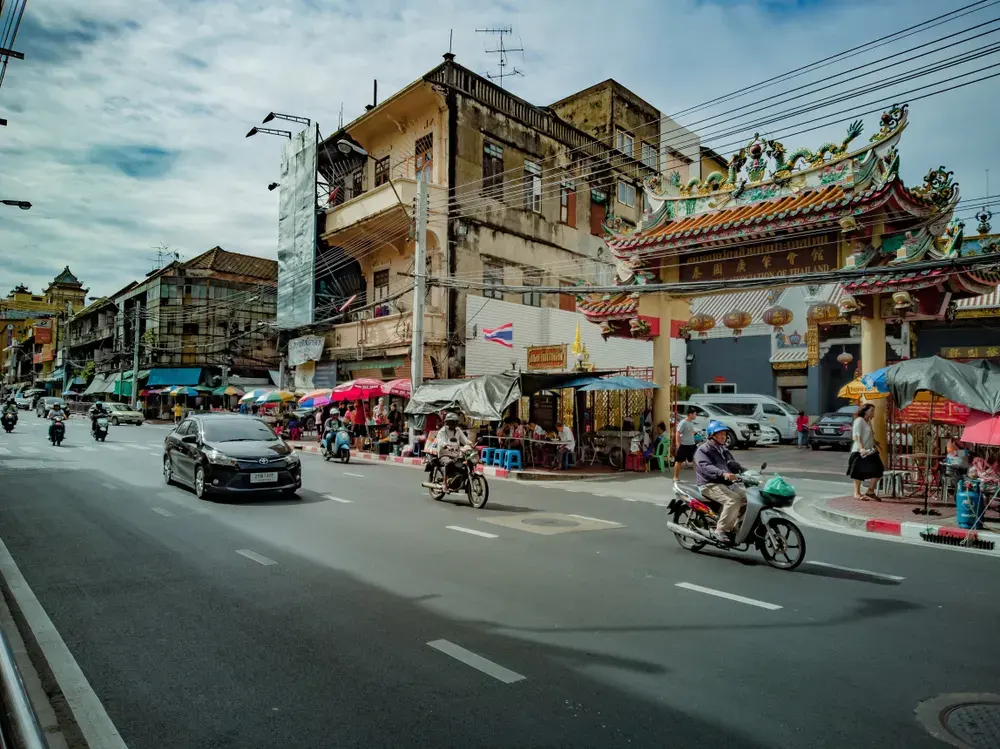 A lively street scene featuring Asian architecture, people, and vehicles on a sunny day.
