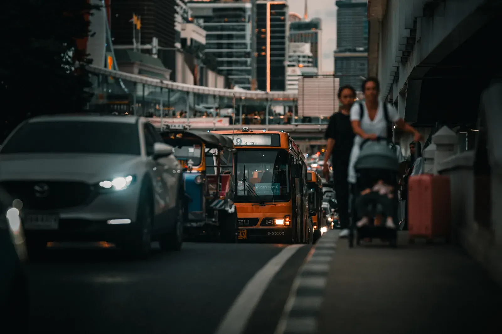 A bustling street in Bangkok, Thailand, with traffic and pedestrians at dusk, showcasing urban life.
