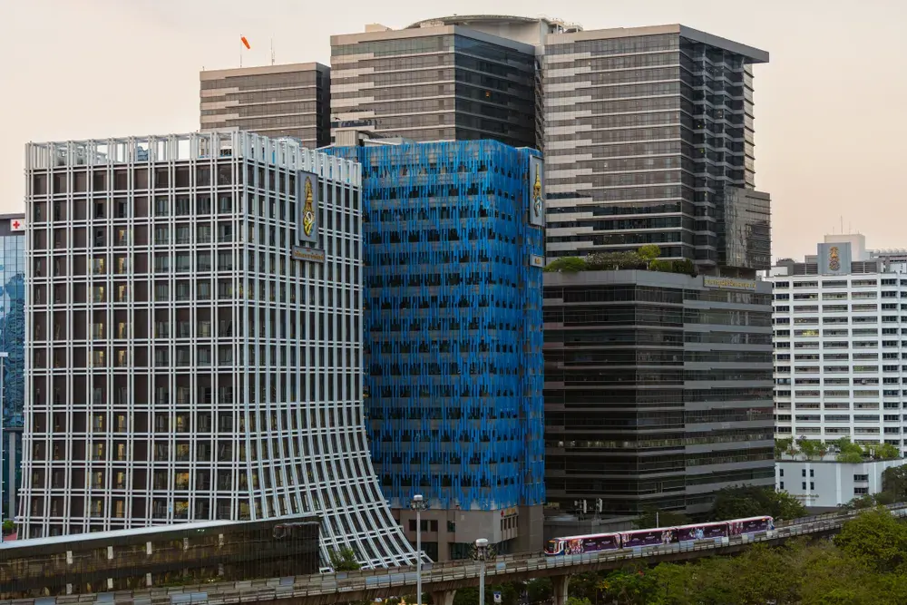 An urban scene of Bangkok's skyline featuring modern architecture and the BTS Skytrain at sunset.